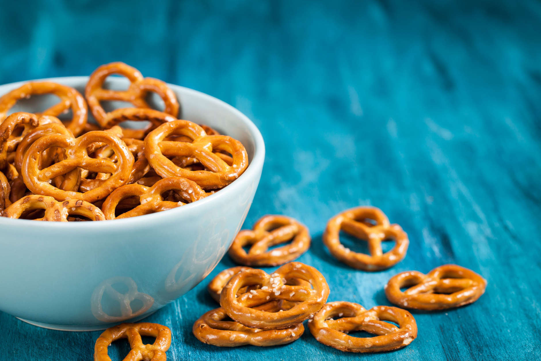Salty snacks mini pretzels in bowl on blue wooden table