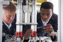 Engineer And Apprentice Working On Machine In Factory