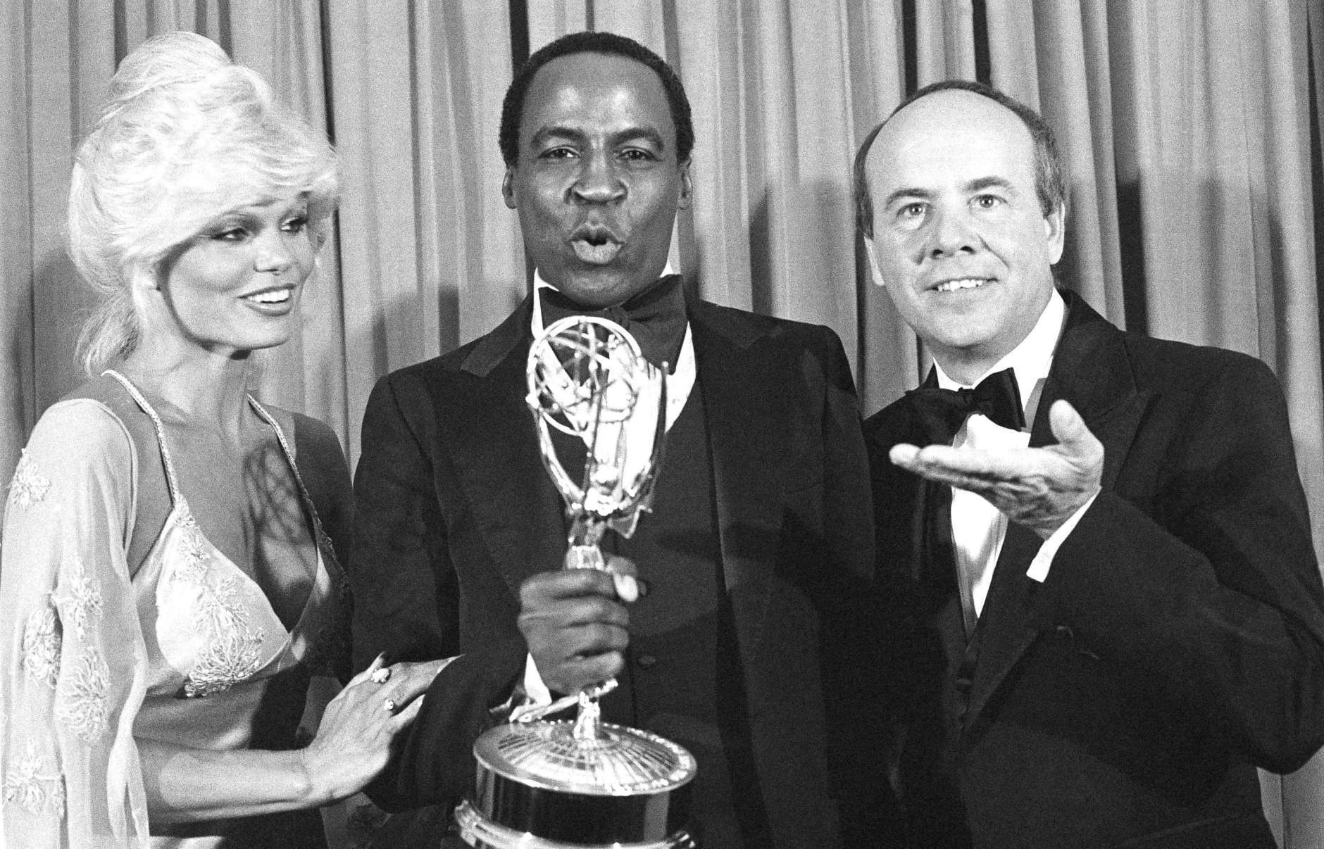 FILE - In this Sept. 10, 1979 file photo, Robert Guillaume, center, accepts his Emmy Award  for best supporting actor in a comedy-variety or music series for his role in "Soap" from Tim Conway, right, and Loni Anderson at the 31st Emmy Awards in Los Angeles.  Guillaume, who won Emmy Awards for his roles on “Soap” and “Benson,” died Tuesday, Oct. 24, 2017 in Los Angeles at age 89. Guillaume’s widow Donna Brown Guillaume says he had been battling prostate cancer. (AP Photo/Reed Saxon, File)