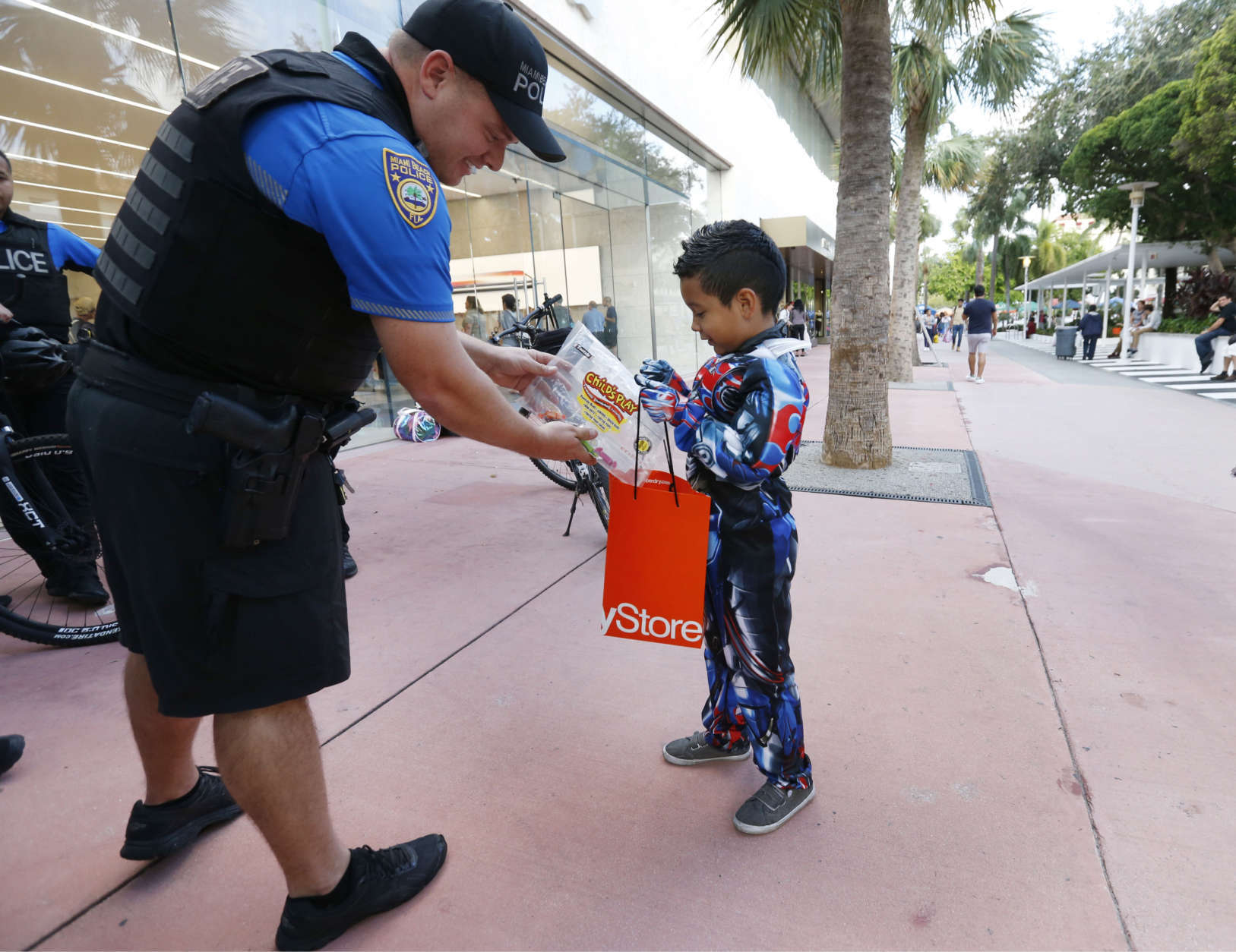 Miami Beach police officer Lee Clair, left, hands out candy to trick-or-treaters like Christopher Rincon, 7, along the Lincoln Road pedestrian mall for Halloween, Tuesday, Oct. 31, 2017, in the South Beach neighborhood of Miami Beach, Fla. (AP Photo/Wilfredo Lee)