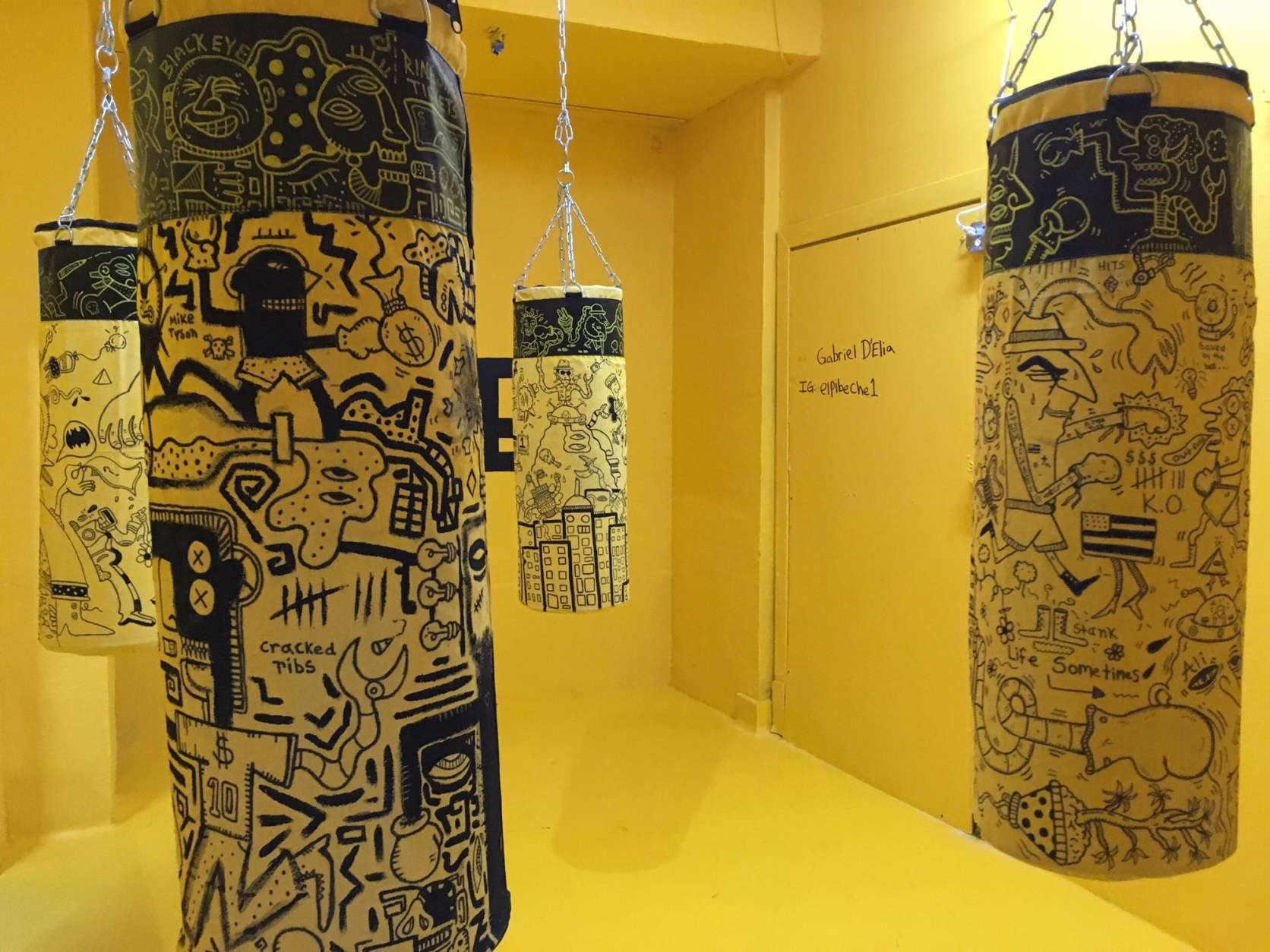 Punching bags designed by Gabriel D'Elia hang in the yellow boxing room. (WTOP/Noah Frank)