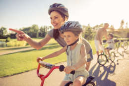 Happy family is riding bikes outdoors and smiling. Parents are teaching their children. Mom and daughter in the foreground