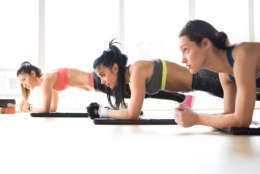 Three attractive sport girls doing plank exercise lying on yoga mat in fitness class.
