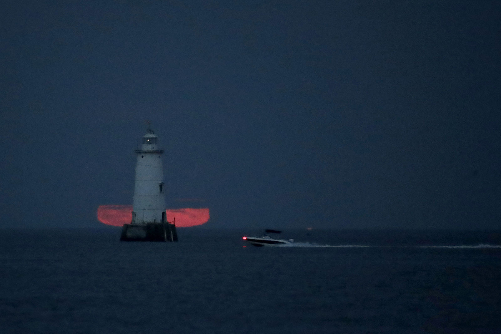A boat cruises in front of the Great Bends Lighthouse as a thick cloud layer obstructs the view of the full moon rising over the Raritan Bay, Thursday, Oct. 5, 2017, in South Amboy, N.J. The moon, better known as the Harvest Moon because it's the first full moon during the fall season, had not risen in its full stage during the month of October since 2009. (AP Photo/Julio Cortez)