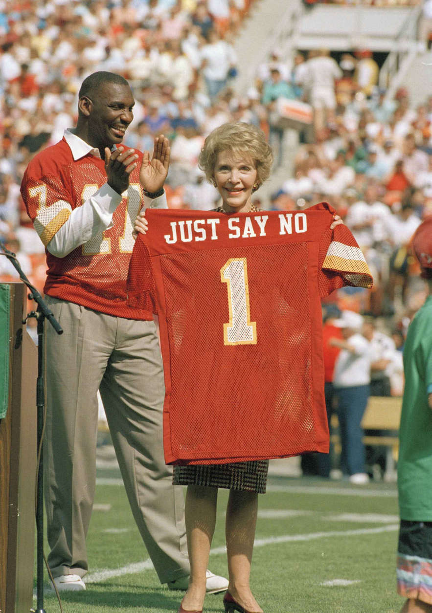 Washington Redskins injured starting quarterback Doug Wiliams stands behind First Lady Nancy Reagan holds a jersey presented to her by Williams prior to the start of game against the New York Giants at RFK Stadium in Washington, D.C., Oct. 2, 1988. The ceremony marked the  Redskins' salute to the First Ladys' "Just Say No' anti-drug campaign. (AP Photo/Doug Mills)