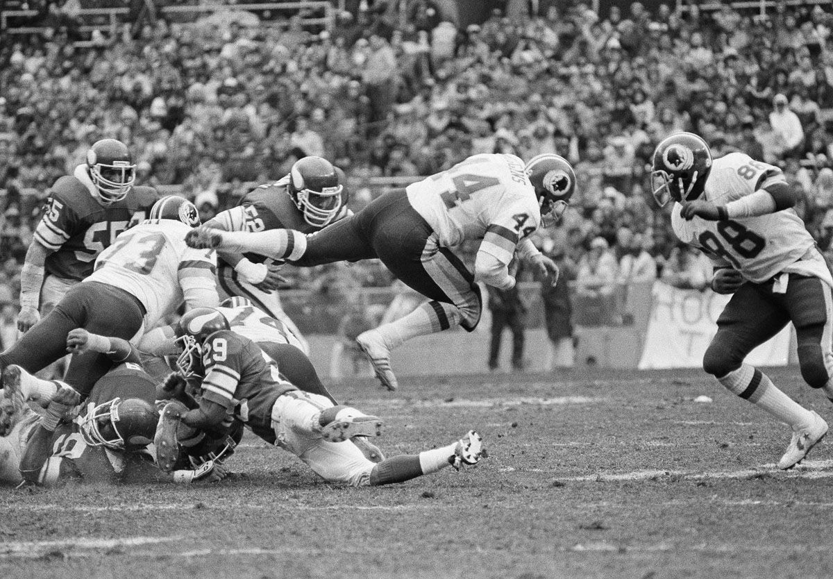 Washington Redskins John Riggins (44) takes to flying as he carries the ball in NFC playoff action against the Minnesota Vikings in Washington, on Saturday, Jan. 15, 1983. Vikings John Swain (29) is on ground. (AP Photo/Ira Schwarz)