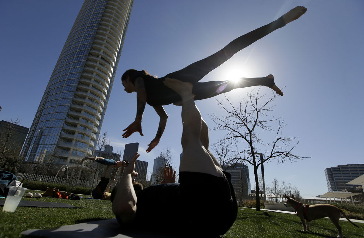 Karla Gallegos is lifted as she practices acro yoga with friends in downtown Dallas, Thursday, Feb. 11, 2016. Spring like weather has moved into Texas making being outdoors during winter enjoyable. (AP Photo/LM Otero)