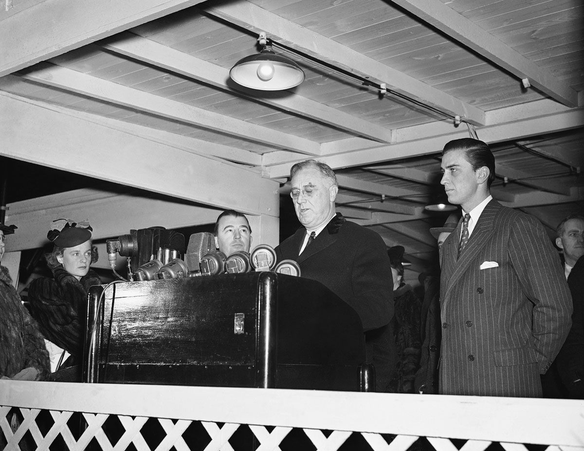 President Franklin Roosevelt is shown above at Christmas-tree lighting ceremony Dec. 24, 1939 in Washington when he thanked god "for the interlude of Christmas" in a torn world. In expressing yuletide greeting to American people, he pushed a button lighting a national Christmas tree back of the White House in Washington, D.C., with President above is his son, Franklin, Jr. (right) and Rep. Jennings Randolph (D-W. Va.), left. (AP Photo)