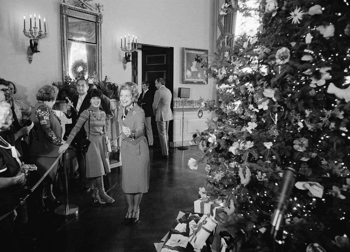 First lady Betty Ford, center left, demonstrates her skiing form for unidentified reporters gathered in the Blue Room of the White House, Dec. 10, 1976. Mrs. Ford gave the reporters a showing of the 1976 White House Christmas tree, right. (AP Photo/Charles Tasnadi)
