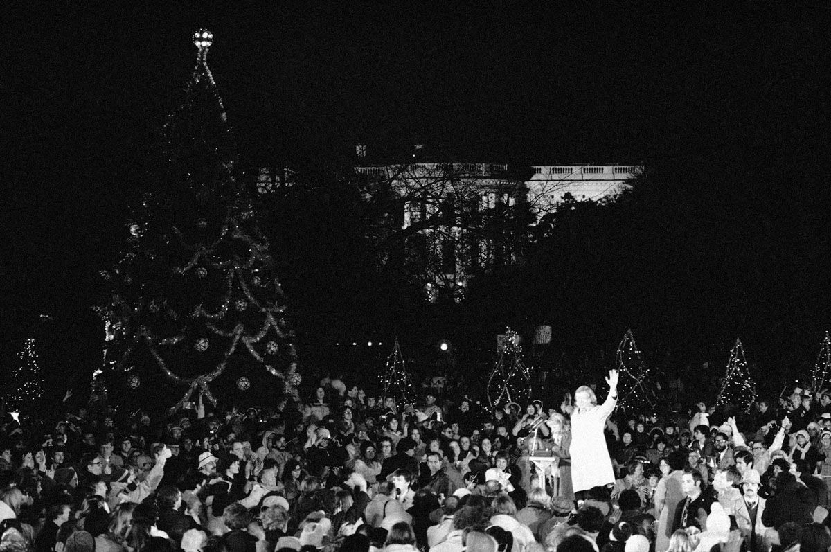 President Jimmy Carter waves after his daughter Amy pushes the button to light the National Christmas Tree on the Ellipse near the White House in Washington on Dec. 13, 1979. To the surprise of the large crowd at the lighting, the president only had the lights on 50 small trees turned on, as well as a star on top of the large tree. Carter said that the rest of the tree’s lights would be turned on after the 50 American hostages were released in Iran. (AP Photo/Dennis Cook)