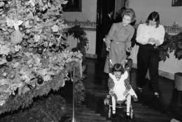 First lady Nancy Reagan takes 5-year-old Amie Garrison of Clarksville, Ind., on a tour of White House Christmas decorations on Monday, Dec. 11, 1984 in Washington. Amie, who is in failing health and in need of a liver transplant, came to Washington with her family to put her favorite ornament on the White House Christmas tree.   Woman at right is not identified.  (AP Photo/Ira Schwarz)