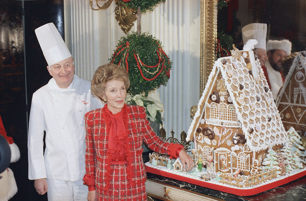 First Lady Nancy Reagan, second from left, touches a gingerbread Rex, her pet dog, who sits next to a little doghouse next to the big White House gingerbread house, Monday, Dec. 15, 1987, Washington, D.C. Mrs. Reagan showed off the house during a tour of the White House Christmas decorations. Reflections of Dom DeLuise, dressed as Santa, and the White House chef can be seen in the mirror. The chef is unidentified. (AP Photo/Barry Thumma)