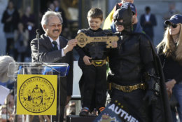 FILE - In this Nov. 15, 2013 file photo, Miles Scott, dressed as Batkid, stands next to Batman as he receives the key to the city from San Francisco Mayor Ed Lee, left, at a rally outside of City Hall in San Francisco. Mayor Lee, who oversaw a technology-driven economic boom in San Francisco that brought with it sky-high housing prices despite his lifelong commitment to economic equality, died suddenly early Tuesday, Dec. 12, 2017, at age 65. (AP Photo/Jeff Chiu, File)