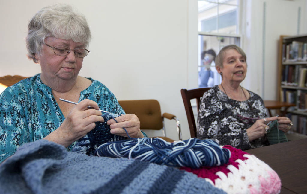 In this photo taken Friday, Nov. 4, 2016, Pat Clement, left, and Christine Hrycuna work on knitting scarves at the Griffin Free Public Library in Auburn, N.H. The two are part of a group that knit around 400 scarves this year and hung them on a park fence for anyone to grab and keep. (AP Photo/Jim Cole)