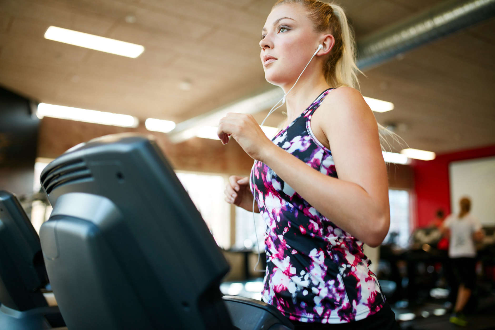 Photo of a fit young woman running on a treadmill in the gym. Caucasian female listening music and exercising on exercise equipment. (Thinkstock)