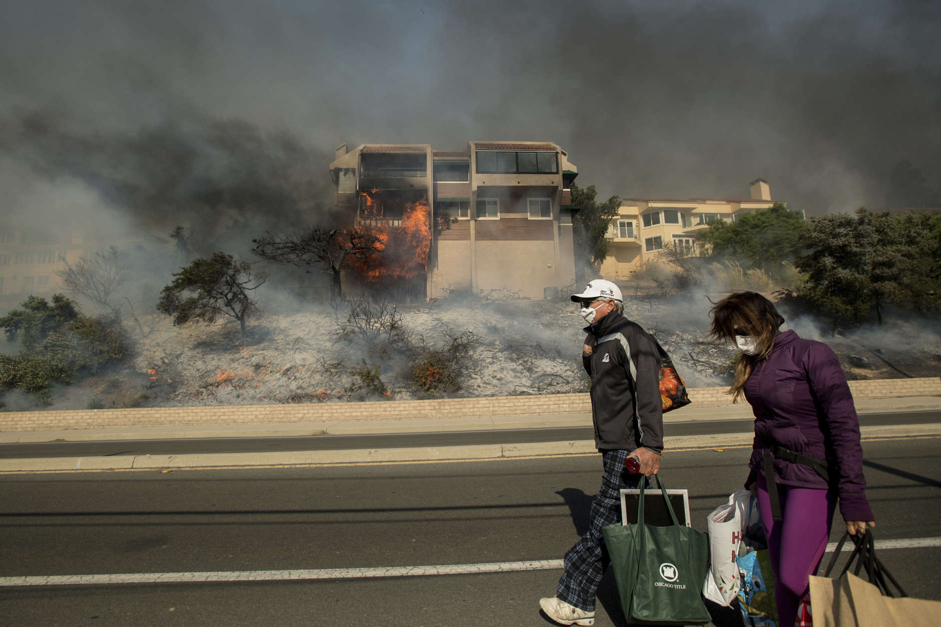 James and Josie Ralstin carry belongings from their Ventura, Calif., home as flames from a wildfire consume another residence on Tuesday, Dec. 5, 2017. The couple evacuated early Tuesday morning as the fire approached, but returned to retrieve medications and other property. (AP Photo/Noah Berger)