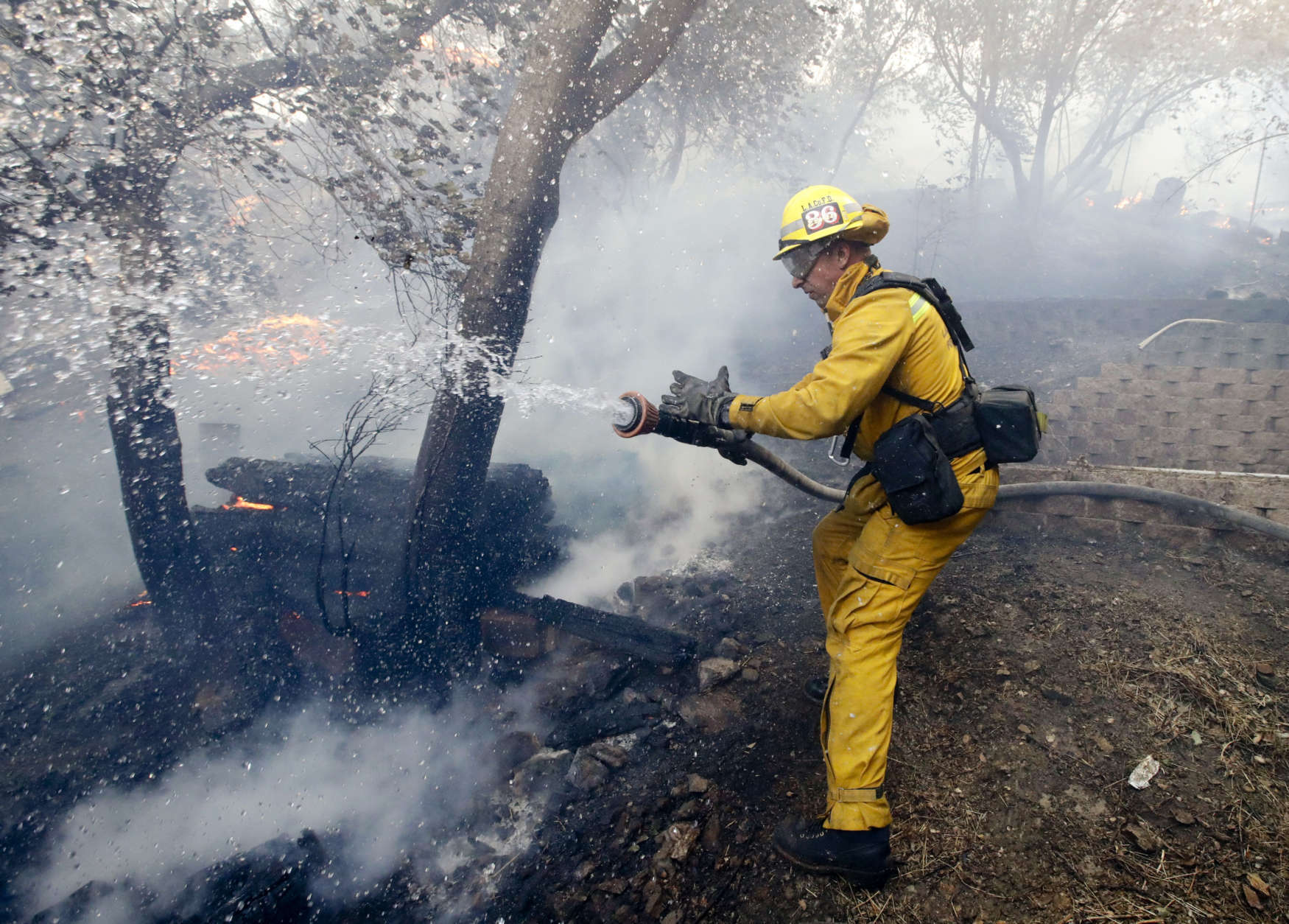 A Los Angeles County firefighter battles a wildfire in the Lake View Terrace area of Los Angeles, Tuesday, Dec. 5, 2017. Ferocious winds in Southern California have whipped up explosive wildfires, burning a psychiatric hospital and scores of other structures. (AP Photo/Chris Carlson)