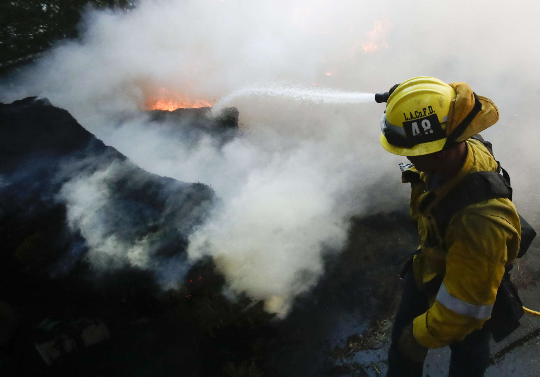 A Los Angeles County firefighter puts water on a burning car during the Creek Fire in the Lake View Terrace area of Los Angeles Tuesday, Dec. 5, 2017. (AP Photo/Chris Carlson)