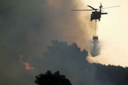 A helicopter drops water while battling the Thomas fire in Ojai, Calif., on Thursday, Dec. 7, 2017.   The biggest and most destructive of the windblown fires raking Southern California shut down one of the region's busiest freeways Thursday and threatened Ojai, a scenic mountain town dubbed "Shangri-La" and known for its boutique hotels and New Age spiritual retreats. (AP Photo/Noah Berger)