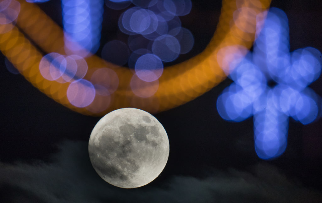 WELLS, ENGLAND - JANUARY 01:  The first full moon of 2018 rises behind festive seasonal lights on display in the High Street in Wells on January 1, 2018 in Somerset, England. Tonight's full moon, which is known by Native American tribes as the "Wolf Moon", is also a supermoon which means it coincides with the Moon's closest approach to Earth, known as the perigee. Tonights Wolf Moon is the first of two full moons in January. The second will take place on the night of January 31 and in some areas of the world this will also happen at the same time as a total lunar eclipse.  (Photo by Matt Cardy/Getty Images)