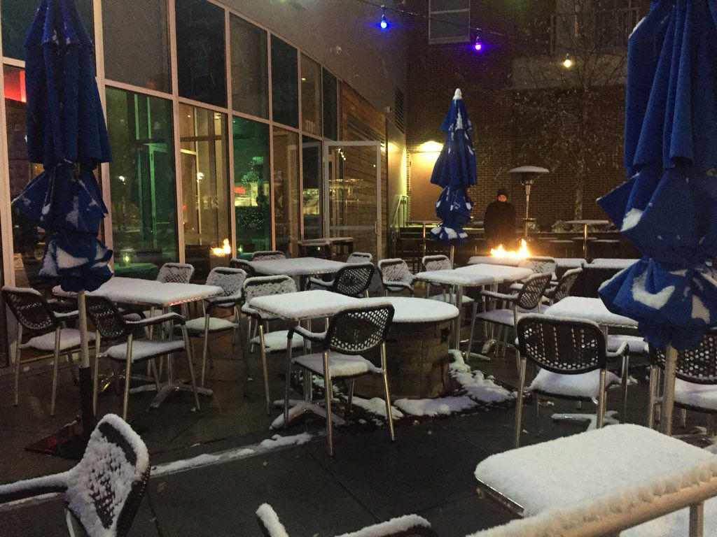 Snow falls on the outdoor dining area of the Grilled Oyster Co. in Northwest D.C. The restaurant's D.C. location is closing but the Maryland one is still open. (WTOP/Patrick Roth)