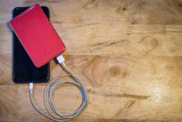 Blank screen smartphone charging with power bank on wooden table.