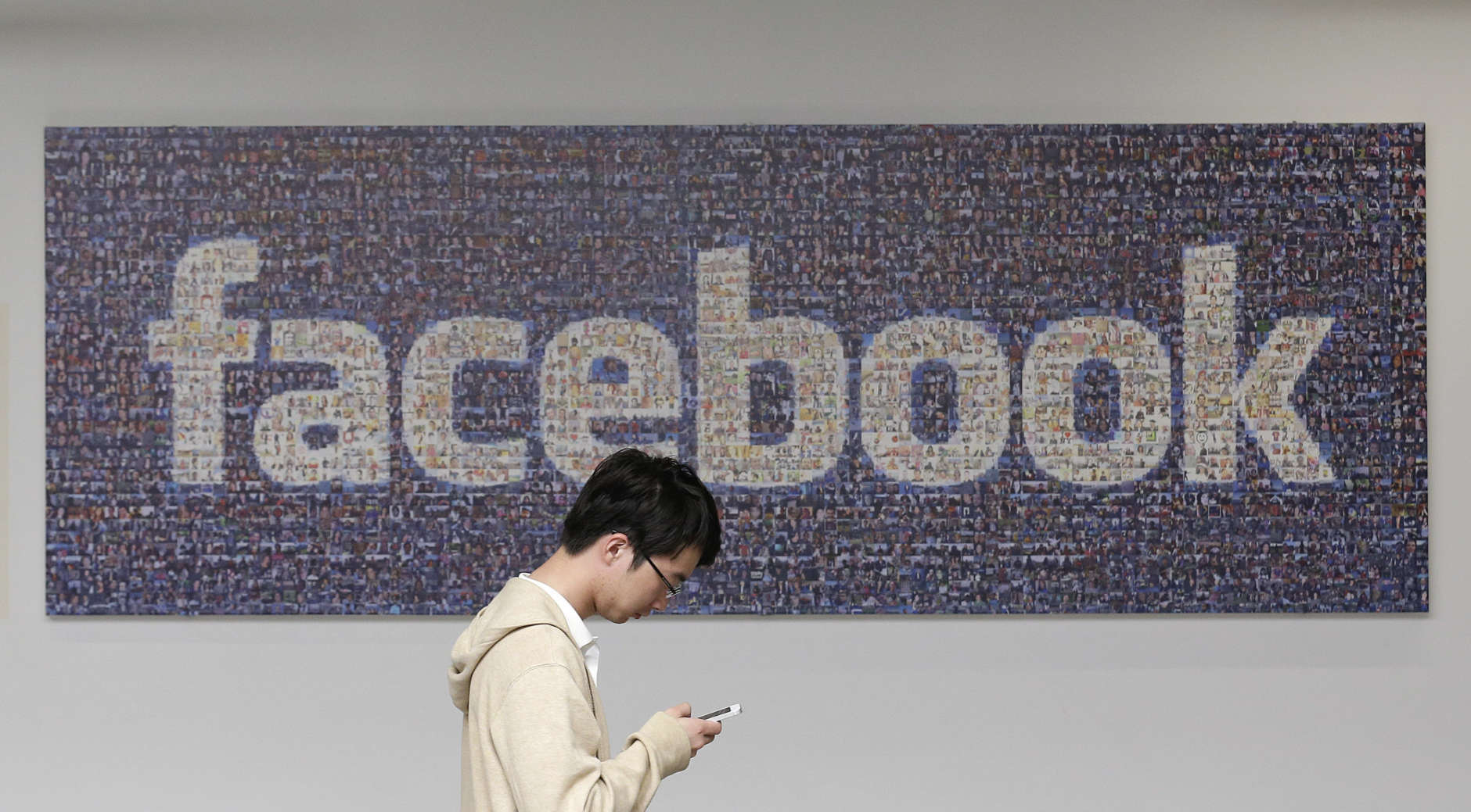 FILE - In this June 11, 2014, file photo, a man walks past a Facebook sign in an office on the Facebook campus in Menlo Park, Calif. Facebook reports financial earnings Wednesday, Jan. 27, 2016. (AP Photo/Jeff Chiu, File)