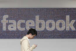 FILE - In this June 11, 2014, file photo, a man walks past a Facebook sign in an office on the Facebook campus in Menlo Park, Calif. Facebook reports financial earnings Wednesday, Jan. 27, 2016. (AP Photo/Jeff Chiu, File)