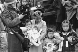 FILE - In this March 30, 1942 file photo, Cpl. George Bushy, left, a member of the military guard which supervised the departure of 237 Japanese people for California, holds the youngest child of Shigeho Kitamoto, center, as she and her children are evacuated from Bainbridge Island, Wash. Roughly 120,000 Japanese immigrants and Japanese-Americans were sent to desolate camps that dotted the West because the government claimed they might plot against the U.S. (AP Photo/File)