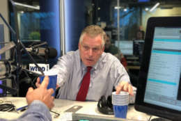 Virginia Gov. Terry McAuliffe hands a cup with stout to WTOP anchor Mark Lewis during "Ask the Governor" on Friday, Dec. 22, 2017. (WTOP/Omama Altaleb)