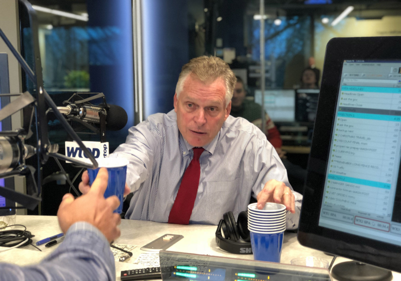 Virginia Gov. Terry McAuliffe hands a cup with stout to WTOP anchor Mark Lewis during "Ask the Governor" on Friday, Dec. 22, 2017. (WTOP/Omama Altaleb)