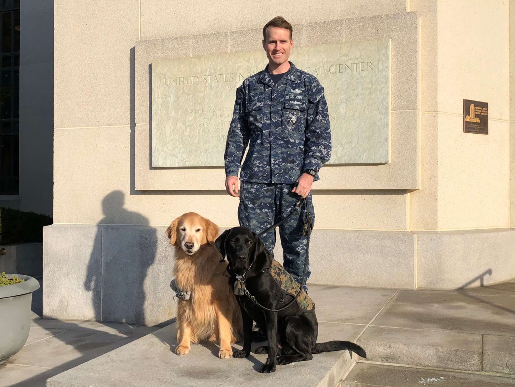 Hospital Corpsman First Class Robert Park pose with Walter Reed National Military Medical Center facility dogs Goldie and Dillon. (WTOP/Kate Ryan)