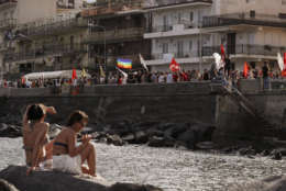 Sunbathers look at demonstrators during an anti-G7 rally near the venue of the G7 summit in the Sicilian town of Taormina, Italy, Saturday, May 27, 2017. A summit of the leaders of the world's wealthiest democracies has ended without a unanimous agreement on climate change, as the Trump administration plans to take more time to say whether the U.S. is going to remain in the Paris climate deal. (AP Photo/Gregorio Borgia)