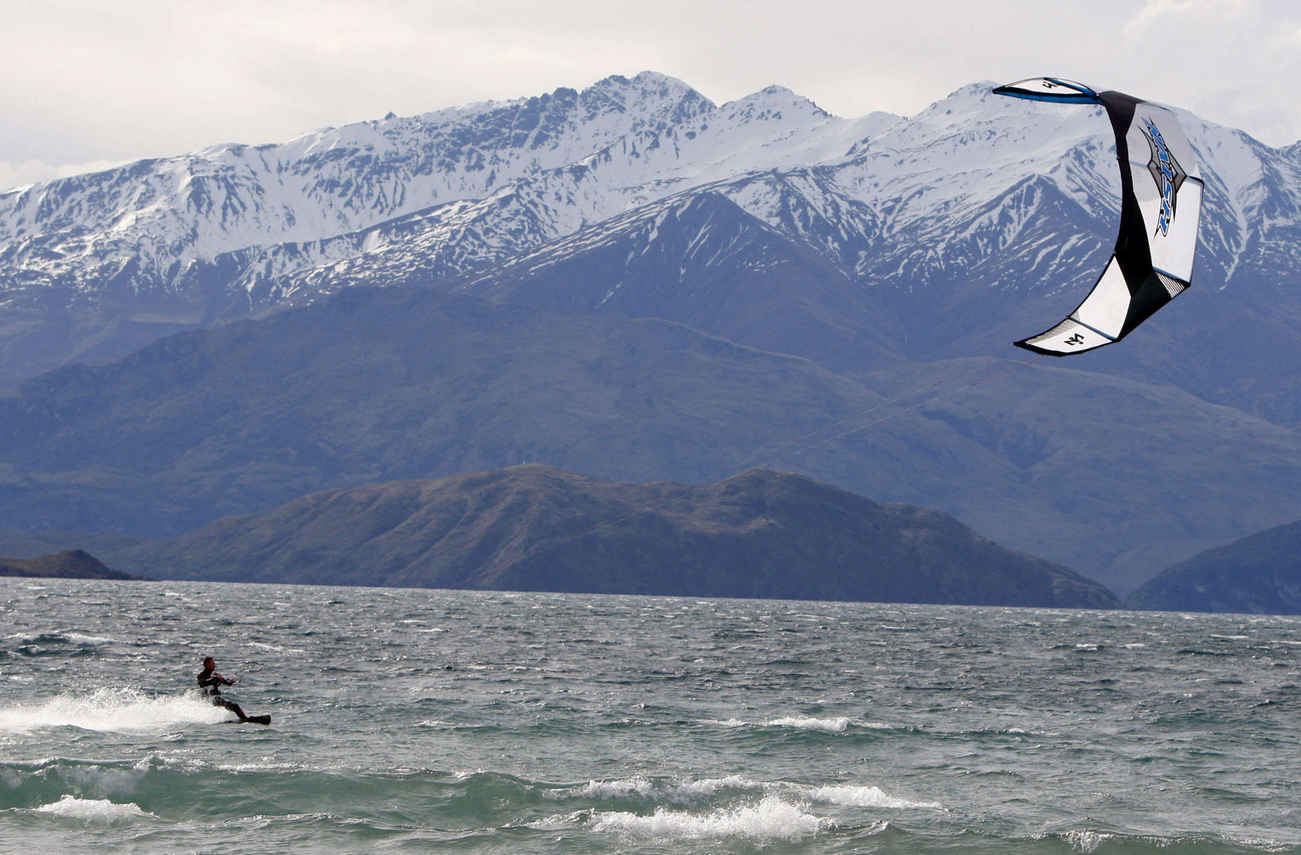 A kite surfer races across Lake Wanaka with the snow capped mountains of the Southern Alps behind as he makes the most of strong north westerly winds that buffeted the ski resort town of Wanaka in New Zealand's South Island, Saturday, Oct. 4, 2008. (AP Photo/Mark Baker)