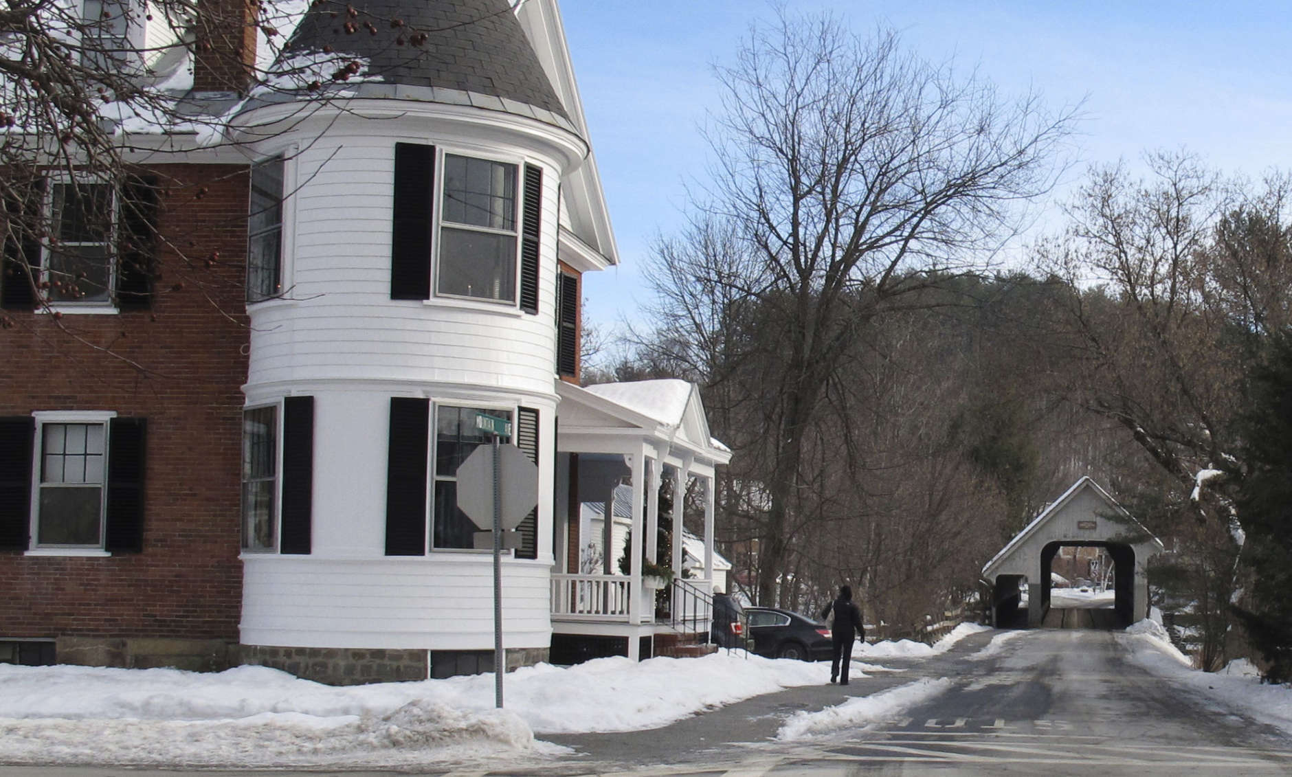 In this photo taken Dec. 20, 2016, a person passes a home with window shutters while walking towards a covered bridge in Woodstock, Vt. The village of Woodstock is cracking down on homeowners who are refusing to keep shutters on their homes. Officials say the loss of shutters would hurt the village's historic character. (AP Photo/Wilson Ring)