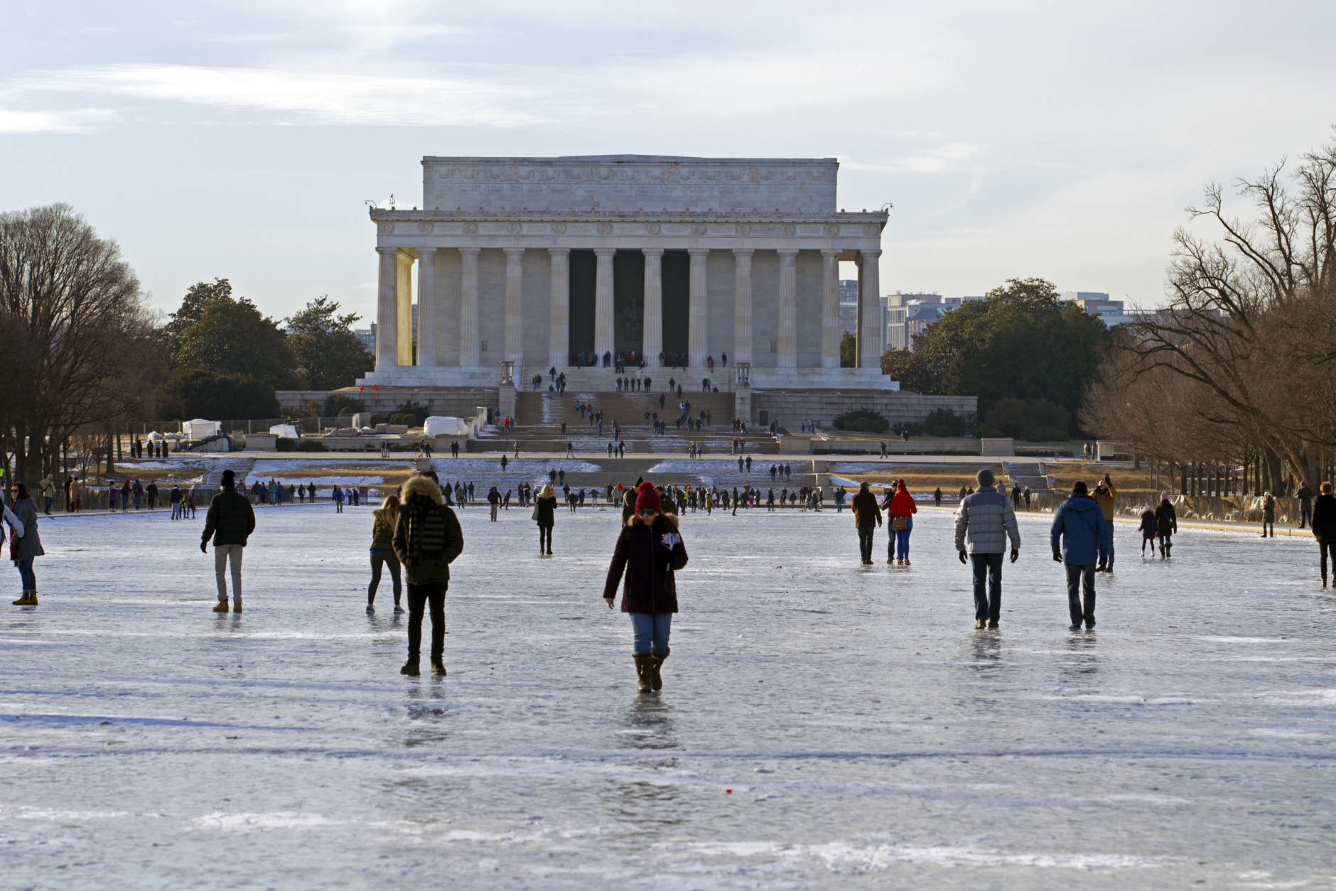 People walk one the frozen Reflecting Pool at the National Mall, Sunday, Jan. 7, 2018, in Washington. The bitter cold that followed a massive East Coast snowstorm should begin to lessen as temperatures inch up and climb past freezing next week. ( AP Photo/Jose Luis Magana)