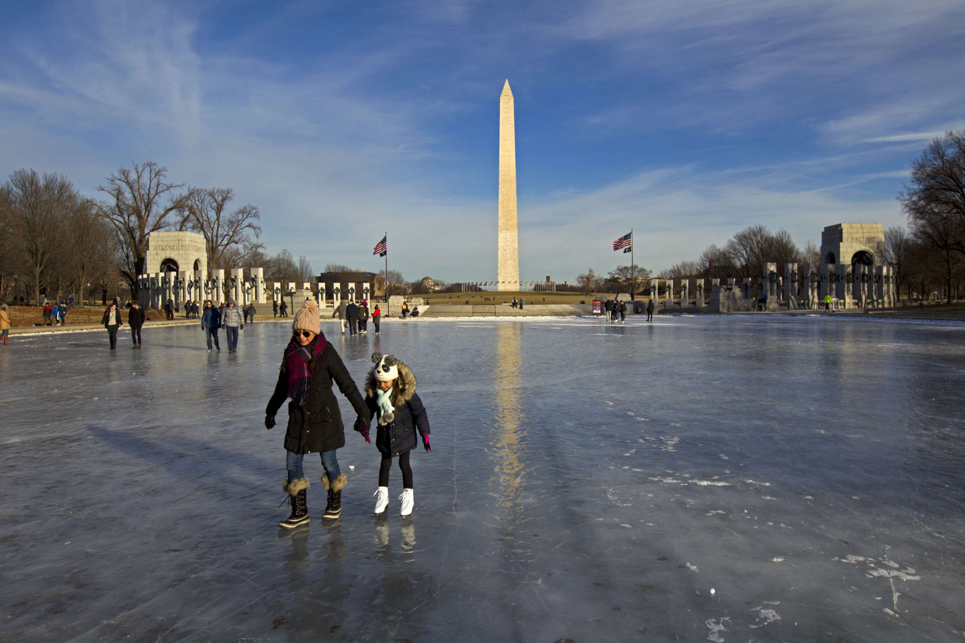 People walk and skate one the frozen Reflecting Pool at the National Mall, Sunday, Jan. 7, 2018, in Washington. The bitter cold that followed a massive East Coast snowstorm should begin to lessen as temperatures inch up and climb past freezing next week. ( AP Photo/Jose Luis Magana)
