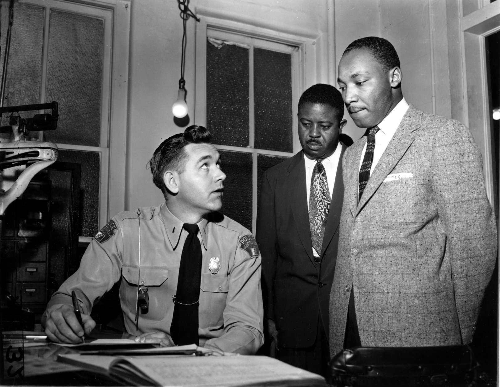 The Rev. Martin Luther King Jr., right, accompanied by Rev. Ralph D. Abernathy, center, is booked by city police Lt. D.H. Lackey in Montgomery, Ala., on Feb. 23, 1956.  The civil rights leaders are arrested on indictments turned by the Grand Jury in the bus boycott.  (AP Photo/Gene Herrick)