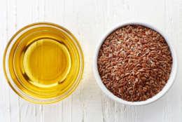 Linseed oil and bowl of linseeds on white wooden background. Top view
