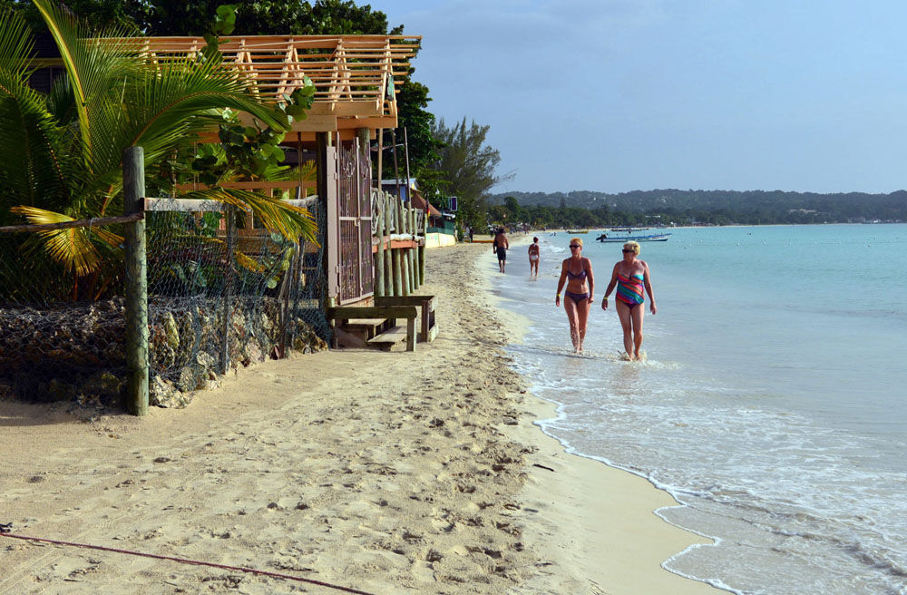 FILE - In this Sept. 14, 2014, file photo, sunbathers walk along a badly eroding patch of resort-lined crescent beach in Negril in western Jamaica. While some islands in the Caribbean were hard-hit by this season's hurricanes, others were relatively unscathed and are open for business as usual. (AP Photo/David McFadden, File)