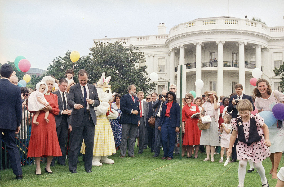 Vice-President and Mrs. Barbara Bush, standing left, watch as a young child starts the annual White House Easter Egg roll, Monday, April 20, 1987 in Washington on the South Lawn of the White House. Some 37,000 people attended the 109th Easter Egg roll. (AP Photo/Ron Edmonds)