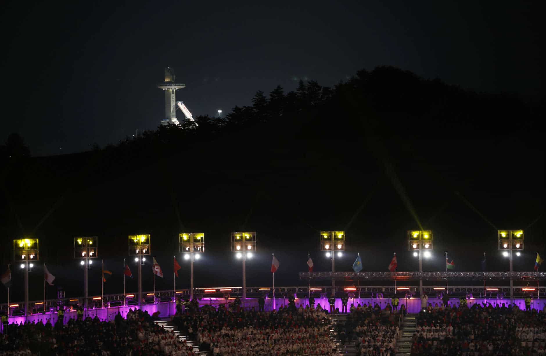 The Alpensia Ski Jumping Center towers are illuminated in the background while people attend the closing ceremony of the 2018 Winter Olympics in Pyeongchang, South Korea, Sunday, Feb. 25, 2018. (AP Photo/Charlie Riedel)