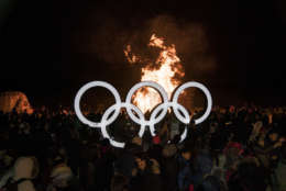People gather around the Olympic rings as an art installation burns in the background at the Fire Art Festival during the 2018 Winter Olympics in Gangneung, South Korea, Saturday, Feb. 10, 2018. The Gangneung coastal cluster is hosting the ice sports, including ice hockey, figure skating, speed skating, short track and curling. (AP Photo/Felipe Dana)