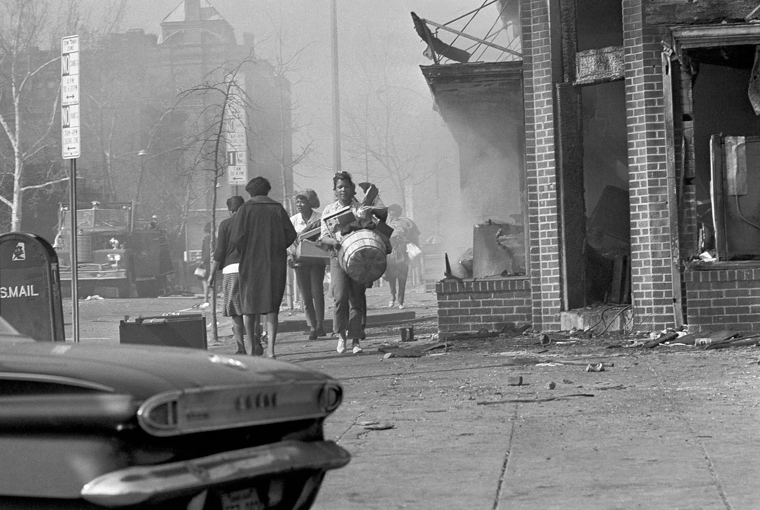 Women carry armloads of clothing and other articles as they walk past a northwest Washington area at 7th and U Streets, April 5, 1968. The area, still dimmed by smoke from burning buildings, was one of the hardest hit as looting and arson flared in the nation’s capital. (AP Photo/Bob Schutz)