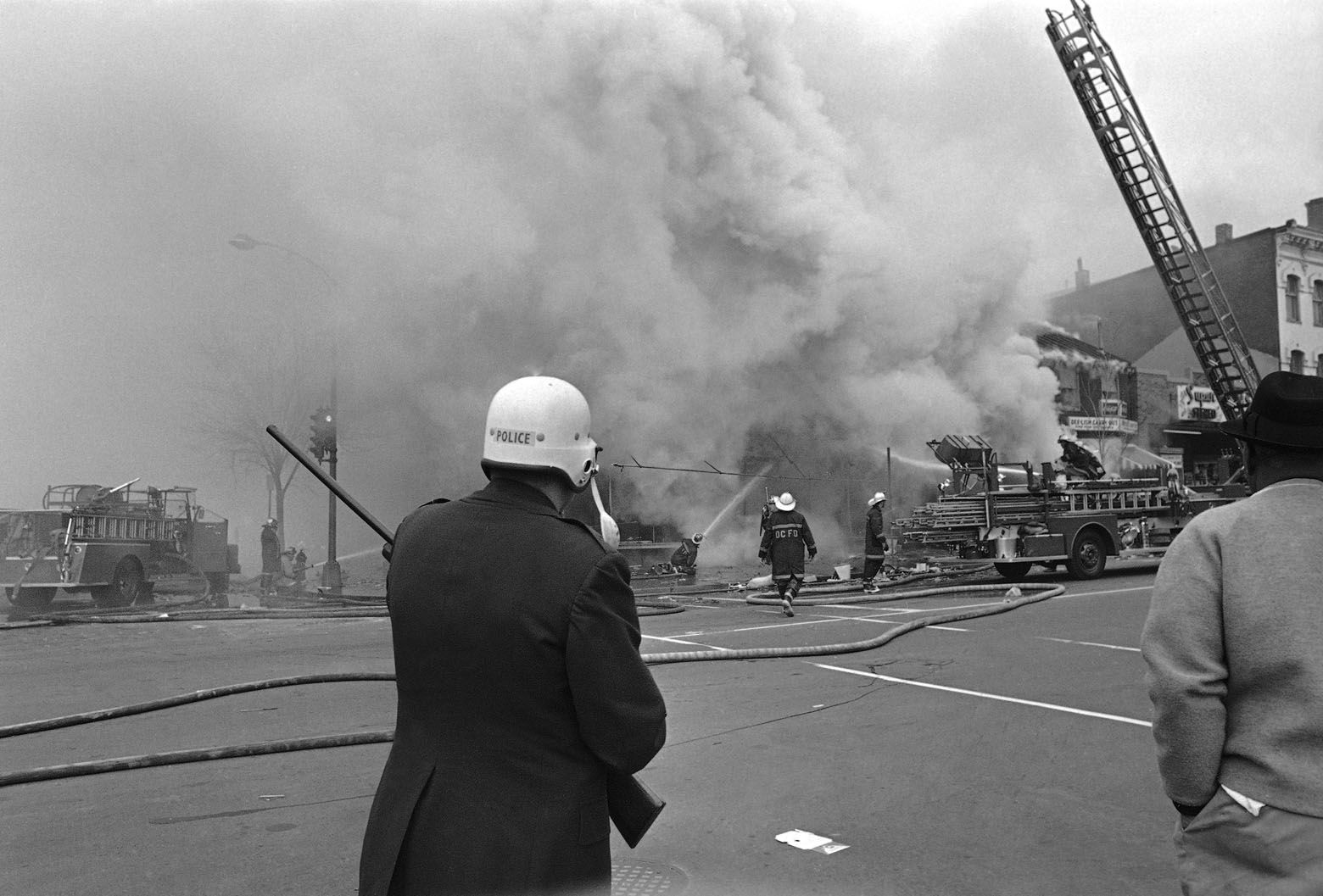 Police stand guard as firemen battle fires in the troubled area of the Capital, Washington, April 6, 1968. The trouble erupted following a night when a curfew was imposed and most burning and looting had subsided. (AP Photo/Charles Tasnadi)