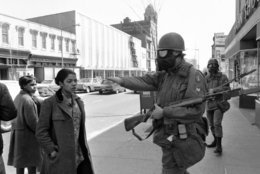 A pedestrian is waved away from a barred area by a gas-masked Army trooper guarding an area near 7th and K Streets, in northwest Washington on April 6, 1968. Another trooper is behind him. Their bayoneted rifles are sheathed. (AP Photo/Bob Schutz)