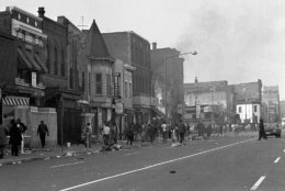 People mill around debris-covered sidewalks on Seventh Street, N.W. near U Street in Washington on April 5, 1968, in a predominantly African American business district. Smoke still rises from building in canter. (AP Photo/Bob Schutz)