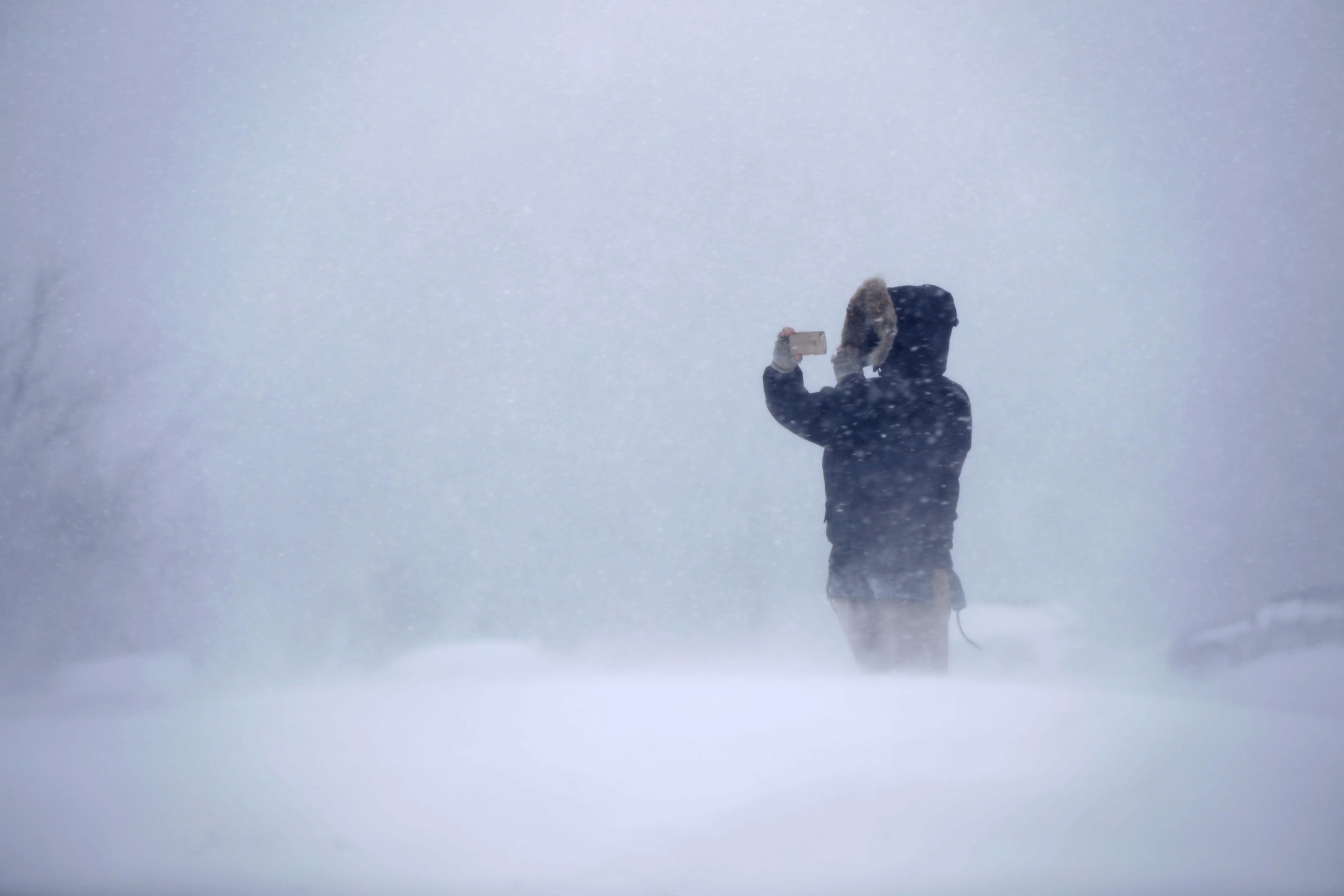 Cassie Peterson uses a phone to record the whiteout conditions during the latest winter storm, Tuesday, March 13, 2018, in Portland, Maine. The third major nor'easter in two weeks slammed the storm-battered Northeast Tuesday with blizzard conditions. (AP Photo/Robert F. Bukaty)