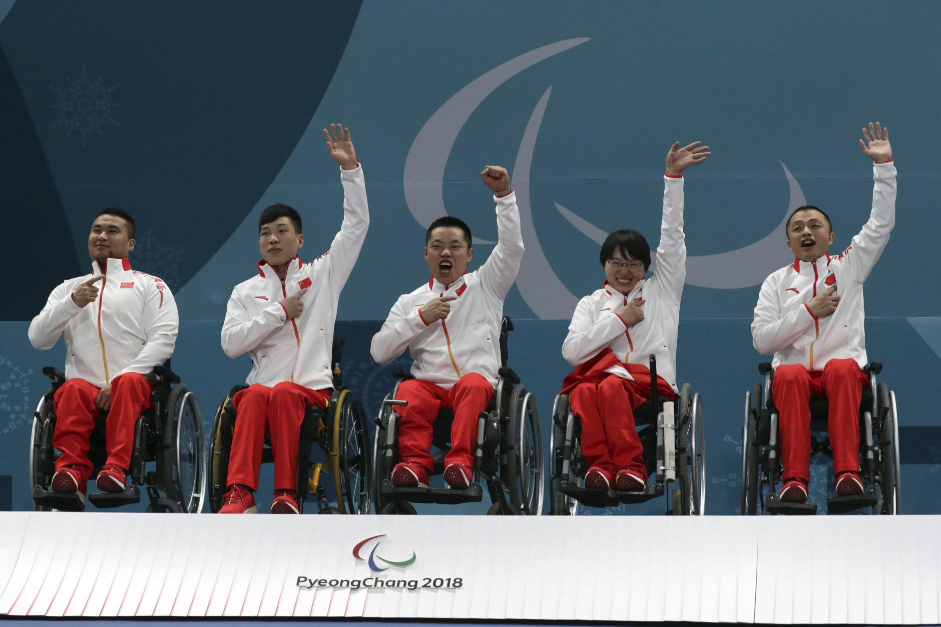 Members of China's wheelchair curling team from left Wang Haitao, Chen Jianxin, Liu Wei, Wang Meng and Zhang Qiang point to their national flag on their jacket as they celebrate on the podium after defeating Norway in the Wheelchair Curling gold medal match for the 2018 Winter Paralympics at the Gangneung Curling Centre in Gangneung, South Korea, Saturday, March 17, 2018.(AP Photo/Ng Han Guan)
