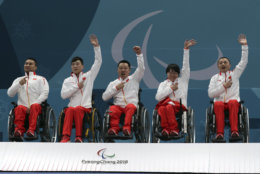 Members of China's wheelchair curling team from left Wang Haitao, Chen Jianxin, Liu Wei, Wang Meng and Zhang Qiang point to their national flag on their jacket as they celebrate on the podium after defeating Norway in the Wheelchair Curling gold medal match for the 2018 Winter Paralympics at the Gangneung Curling Centre in Gangneung, South Korea, Saturday, March 17, 2018.(AP Photo/Ng Han Guan)